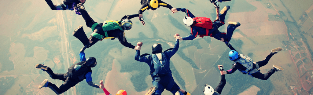 Sky divers in team formation with arms linked. Team-of-teams culture in IT may require a new operating model but not a new organizational model.
